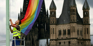 Ein Arbeiter hängt vor der Kulisse des Kölner Doms eine Regenbogenfahne auf