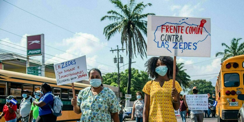 Zwei Frauen tragen Schilder auf einer Demo: Contra las ZEDES