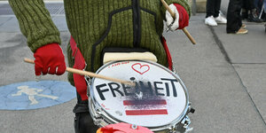 Ein Mensch in grüner Strickjacke trommel mit roten Handschuhe, Freiheit steht auf der Trommel