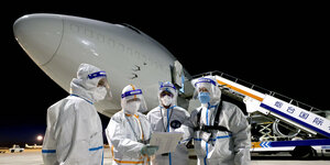 4 Menschen in weißen Schutzanzügen stehen vor einem Flugzeug