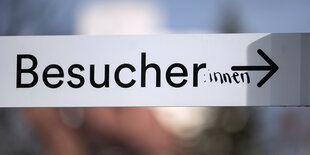 Ein "Besucher"-Schild, das mit einem handgeschriebenen Zusatz zum "Besucher:innen"-schild gemacht wurde