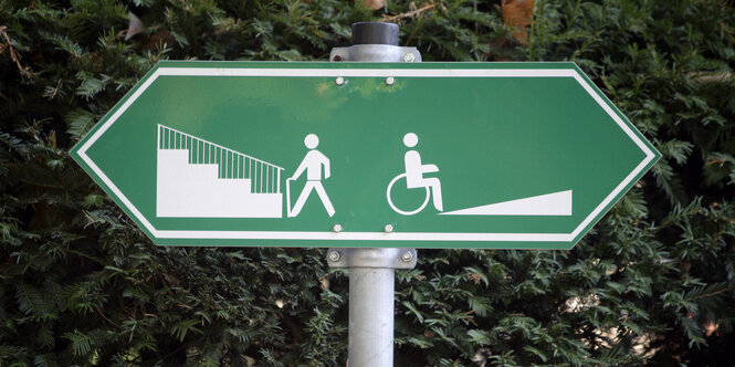 Schild mit Pfeil in beide Richtungen: links zur Treppe mit gehendem Mensch, rechts zur Rampe mit Mensch im Rollstuhl