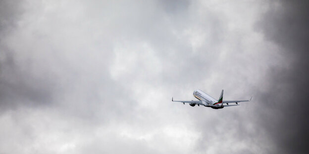 Steigendes Flugzeug vor grauen Wolken.