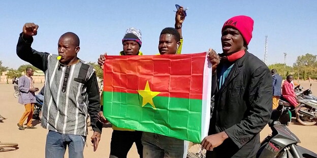 3 Männer halten die Fahne von Burkina Faso,ein gelber Stern in rot und grün, Einer reckt die Faust und trillert auf einer Pfeife