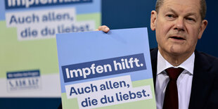 Olaf Scholz hält Werbetafel für die neue Impfkampagne hoch