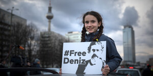 Junge demonstrantin mit dunklen Zöpfen hält auf einem Auto ein Schild "FreeDeniz