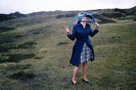 Eine Frau in blauem Regenmantel auf Sylt, sie lässt ihr buntes Kopftuch im Wind flattern