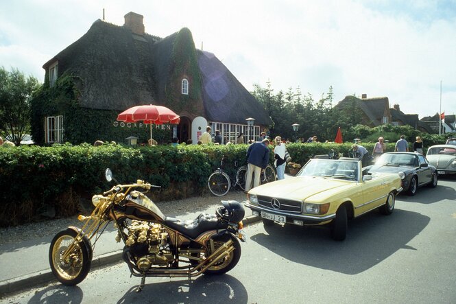 Vor dem Restaurant Gogärtchen auf Sylt parken ein vergoldeter Chopper, ein Mercedes-Cabrio und ein Porsche