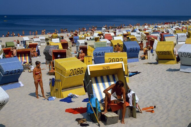 Die Szene am Strand von Westerland zeigt bunte Strandkörbe und braun gebrannte Menschen zur Sommerferienzeit. Der Himmel ist blau, das Meer auch