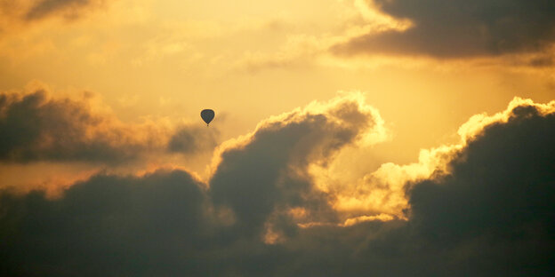 wolkiger Himme, mit schönem orangenem Sonnenuntergang, im Vordergrund ein fliegender Heißluftballon