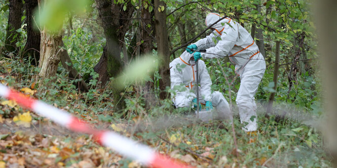 Zwei Menschen im Schutzanzug stehen in der Natur und nehmen Erdproben.