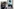 Ein Polizist steht vor einem Polizeiwagen und raucht daneben geht ein alter Mann vor einem Werbeplakat mit Frauen Portrait