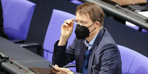 Karl Lauterbach nimmt seine Brille ab und sitzt im Deutschen Bundestag