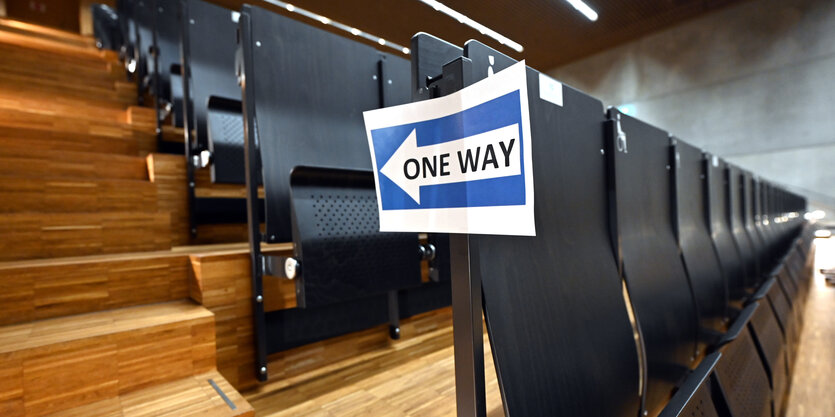 Ein leerer Hörsaal, am Rande einer Sitzreihe ein Schild "One way", dass auf die Einbahnstraßenregelung beim Betreten hinweist.