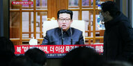 Personen stehen vor einerm Fernsehschirm in dem Kim Jong Un spricht