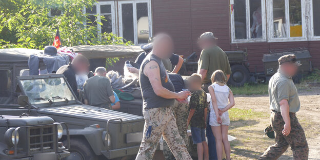 Ein Mann in Camouflage-Hose, verpixelt, im Hintergrund beugen sich andere Personen über Militärfahrzeuge und Uniformen