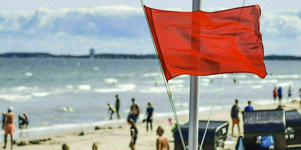 Eine rote Badeverbotsflagge an einem Strand mit Menschen