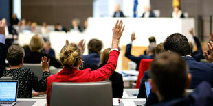 Eine Frau mit einer roten Jacke fällt zwischen anderen Abgeordneten im Parlament auf