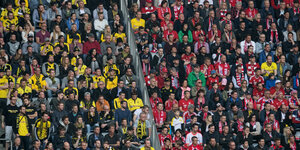 Fans von Bayern München und Borussia Dortmund sitzen im Stadion in getrennten Sitzblöcken.