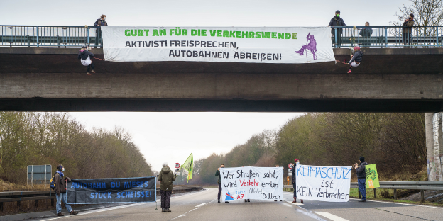 Mehrere Aktivist:innen seieln sich von einer Autobahnbrücke ab und halten Transparente