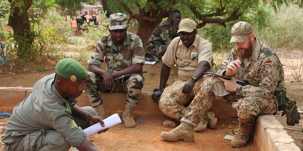 Malische Soldaten und ein deutscher Ausbilder sitzen bei einer Besprechung beieinander