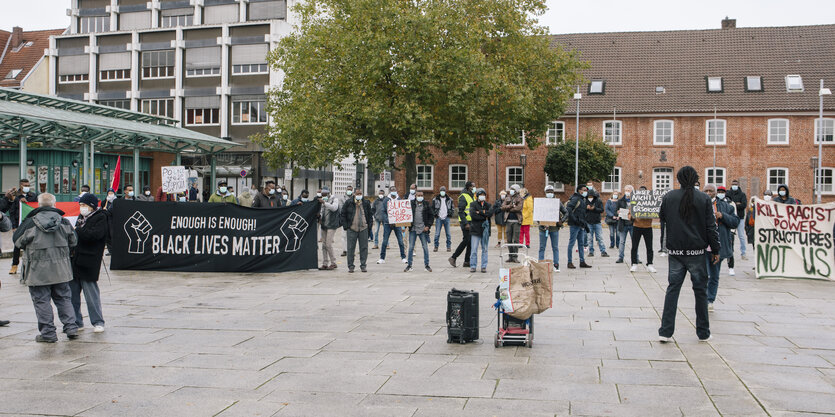 Menschen stehen auf dem Rathausplatz in Stade und halten ein "Black Lives Matter"-Banner