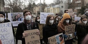 Menschen stehen in einer Reihe und halten Protestplakate in den Händen