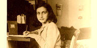 Anne Frank sitzt an einem Schreibtisch