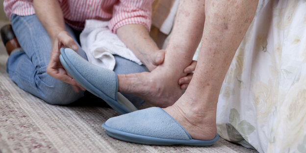 Pflegekraft hilft einer alten Frau, die Pantoffeln auszuziehen
