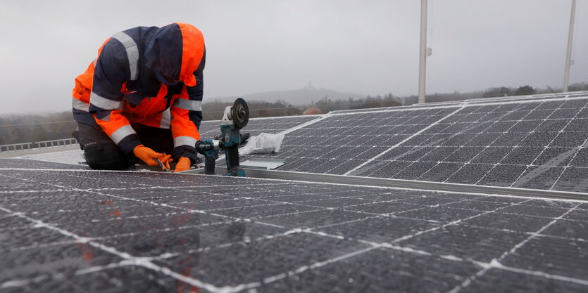 Mann kniet schraubend auf einem flachen Dach mit Solarpanelen