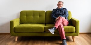 Gerhard Trabert sitzt mit überschlagenen Beinen auf einem grünen Sofa vor einer weißen Wand