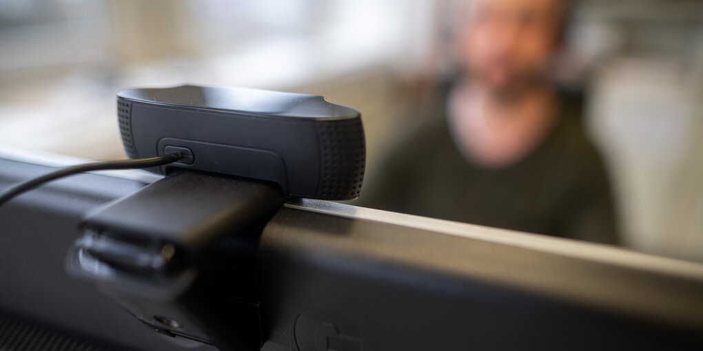 Ein junger Mann sitzt hinter einem Computerbildschirm mit Kamera.