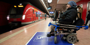 ein Rollstuhlfahrer wartet auf einen einfahrenden roten Zug