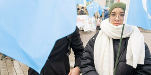 Eine Frau mit Kopftuch und hellblauer Fahne auf einer Demo