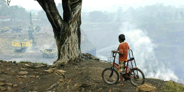Ein kleiner Junge auf einem Fahrrad blickt auf eine Kohletagebau in Indien
