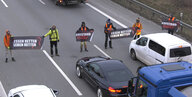 Aktivist*innen stehen mit einem Transparent vor stehen Fahrzeugen auf der Autobahn