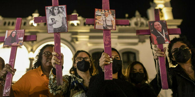 Vier Frauen halten Holzkreuze mit Fotos von Frauen darauf