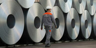 ein Beschäftigter der Salzgitter AG geht an aufgerollten Stahlrollen vorbei