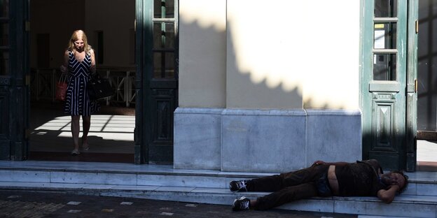 Eine Frau kommt aus der U-Bahnstation Monastiraki. Neben ihr, ein Obdachloser.