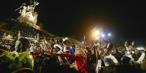 Euphorisch jubende Fans feiern den Sieg und recken ihre Arme in die Höhe, darüber schwebt eine riesige angestrahlte Steinskuptur