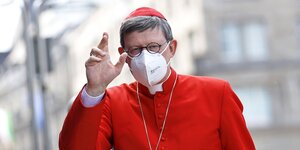 Kardinal Woelki trägt ein rotes Gewand und einen weißen Mundschutz