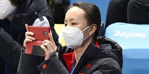 Die chinesische Tennisspielerin Peng Shuai als Zuschauerin beim olympischen Eiskunstlauf. Sie fotografiert mit ihrem Smartphone.