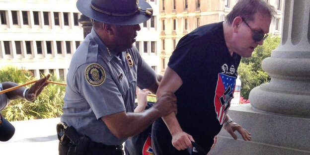 Ein Polizist hilft einem Mann, der ein T-Shirt mit einem Hakenkreuz darauf trägt