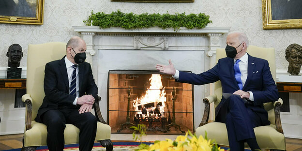 Olaf Scholz und Joe Biden sitzen mit Anzug und Mundschutz vor einem Kaminfeuer