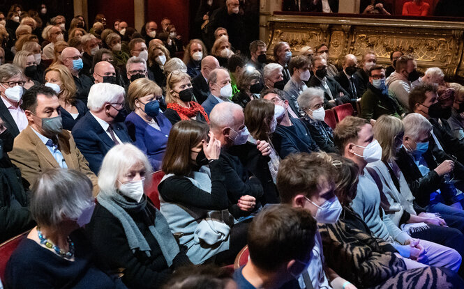 Viele Menschen sitzen mit Maske eng gedrängt im Theater