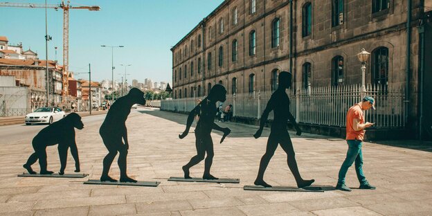 Vier Statuen und ein Mensch bilden die evolutionäre Entwicklung des Menschen ab