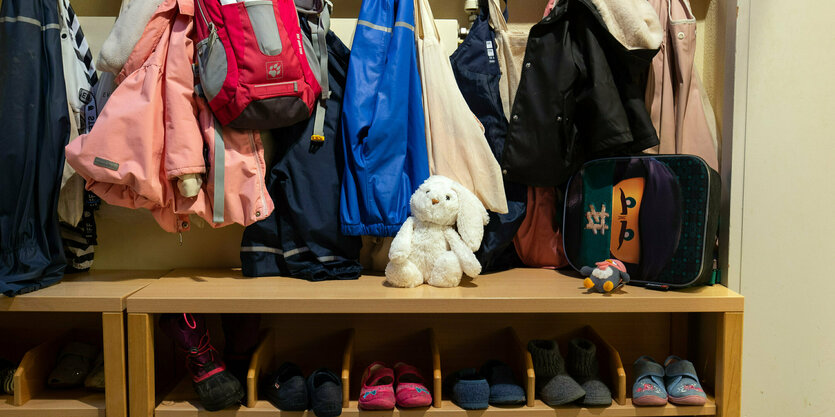 Kinderschuhe und Kinderkleider , eine Kita Garderobe, dazwischen ein weißer Plüschhase