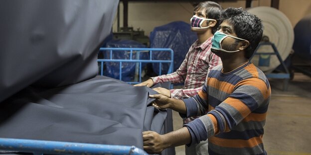 Zwei Textilarbeiter mit Mundschutzmasken vor Stoffbahnen
