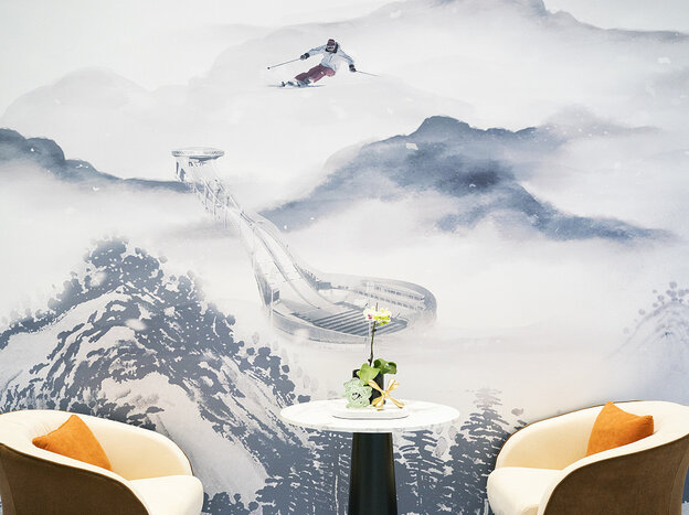 Zwei Stühle und ein Tisch stehen vor einem Wandbild, das eine Schneelandschaft und einen Skifahrer zeigt