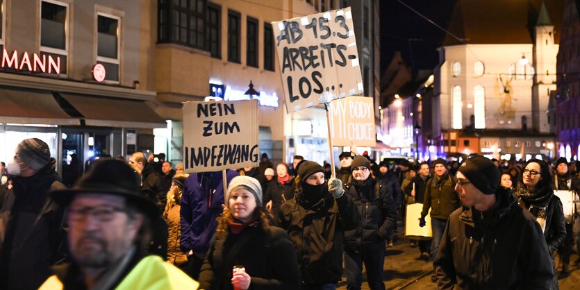 Coronaleugner halten bei einer Demonstration am Abend Plakate hoch und drohen mit Arbeitslosigkeit ab 15. März